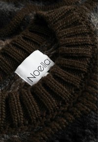 Tamsiai rudas megztinis su neryškiu apykakle; turi baltą etiketę su "Noella" juodu tekstu, siuvinėtą į iškirptę.