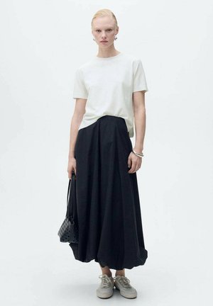 Witte T-shirt met korte mouwen, gecombineerd met een zwarte, lange A-lijn rok. Accessoires bestaan uit een kleine zwarte tas en lichtgrijze sneakers.
