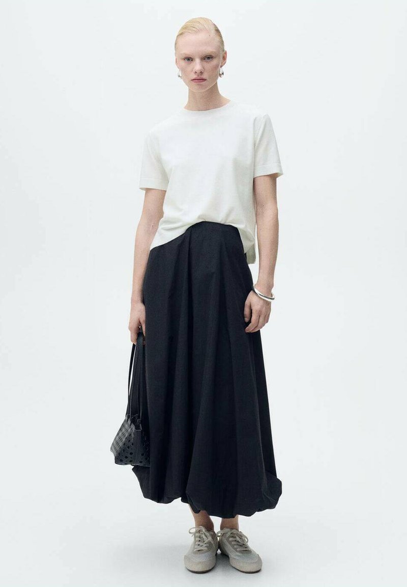 Hvid T-shirt med kortærmer parret med en sort, gulvlængde A-line skirt. Accessories inkluderer en lille sort taske og lysegrå sneakers.