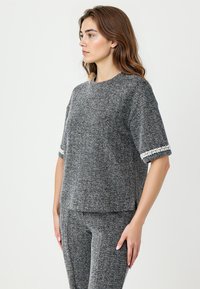 Grijze gebreide top met korte mouwen en witte decoratieve accenten op de manchetten. Relaxed fit, ronde halslijn en zachte stof.