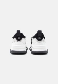 Vue arrière de baskets athlétiques en noir et blanc, présentant des matériaux en mesh et en daim, avec une semelle texturée et des languettes de traction.