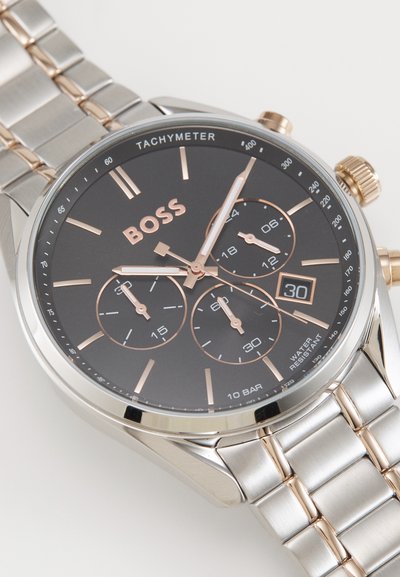 Montre en acier inoxydable argenté avec un cadran noir, des accents en or rose, des sous-cadrans chronographe et un affichage de la date. Résistante à l'eau.