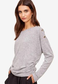 Hallide hall sleeves ja paadi kaelusega hall tops, tekstuurse kangaga ja kolme dekoratiivse nupuga õlal. Rikkalik detail vöökohtade juures.