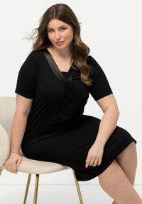 Vestido negro de tela suave, con escote en V y ribete en verde oliva, mangas cortas y un corte relajado.