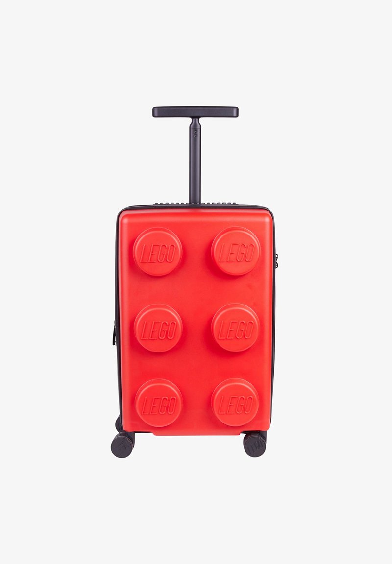 Red hard-shell suitcase with a textured, LEGO brick design, featuring six raised LEGO dots, a retractable handle, and four wheels.