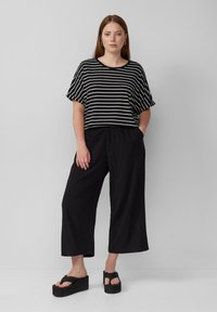 Zwart-wit gestreept T-shirt met korte mouwen, wijdere zwarte broek met elastische tailleband en zwarte platform sandaaltjes met een geweven afwerking.