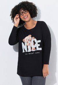Czarny top z długim rękawem z grafiką misia i literami z kryształków, tworzącymi napisy "NICE" oraz "to meet you". Miękki materiał, casualowy krój.