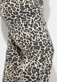Tessuto a fantasia leopardata in crema e nero, con macchie di forme e dimensioni diverse. Il materiale appare testurizzato con dettagli di cucitura visibili.