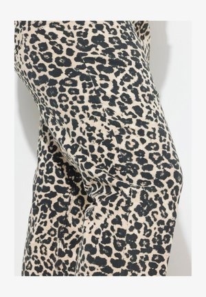 Løveprints stof i creme og sort med varierende pletformer og størrelser. Materialet fremstår struktureret med synlige sy- og detaljedi.