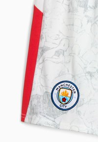 Jersey de tejido blanco con acentos rojos, que presenta un sutil patrón de boceto en gris y un logo redondo del Manchester City bordado en el dobladillo.