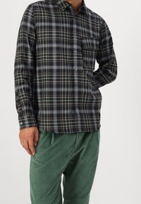 Geruit flanellen overhemd in donkere tinten met blauwe en bruine lijnen, voorzien van een geknoopte voorkant, kraag en een enkele borstzak.