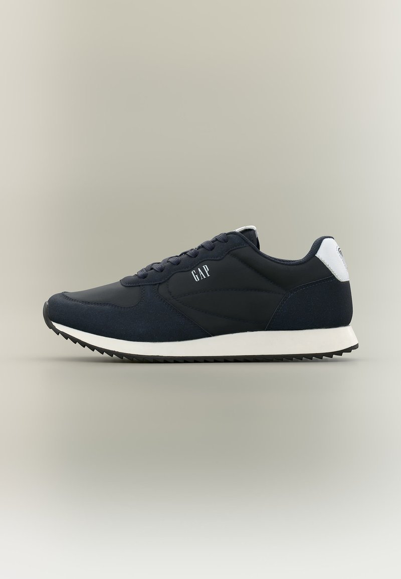 Chaussure de sport bleu marine avec semelle blanche, motif zigzag noir, design à lacets et logo "GAP" sur le côté et la languette arrière.