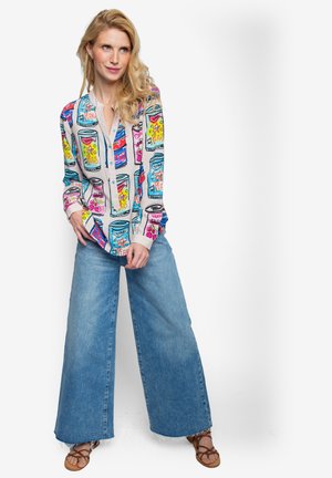 Gedrukt overhemd met knopen met kleurrijke blikjesgraphics, gecombineerd met lichtblauwe denim jeans met wijde pijpen en bruine sandalen.