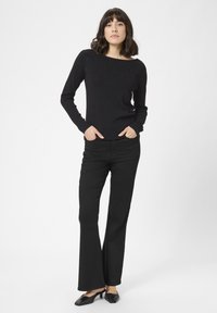 Czarny sweter z długim rękawem w teksturowe kropki, w zestawieniu z czarnymi spodniami dzwonami i czarnymi klapkami na obcasie. Prosty i elegancki design.
