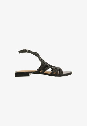 Sandalo piatto nero con cinturini intrecciati, una cinghia alla caviglia con fibbia e una soletta liscia. Design semplice con una suola a profilo basso.