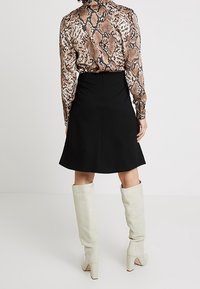 Blouse à manches longues avec un motif imprimé serpent brun et noir, associée à une jupe noire ajustée et des bottes haute-taille gris clair.