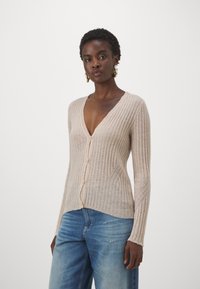 Ribbat beige kofta med djup V-ringning, långa ärmar och knäppning. Ett par ljusblå denimjeans med avslappnad passform och slitna detaljer.