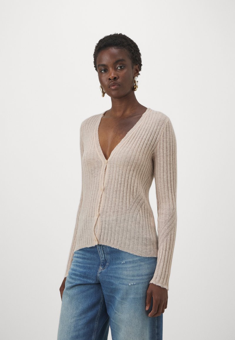Ribbat beige kofta med djup V-ringning, långa ärmar och knäppning. Ett par ljusblå denimjeans med avslappnad passform och slitna detaljer.