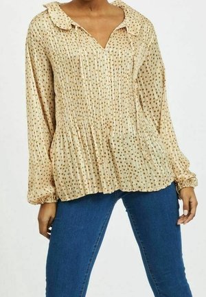 Blouse couleur crème avec un col en V, un design plissé, des manches longues avec des poignets élastiques, et des motifs de points marron dispersés.