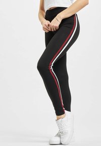 Sorte leggings med røde og hvide sidelister, lavet af strækbart materiale. Sammen med hvide træningssko.