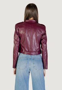 Veste en cuir bordeaux courte avec un design ajusté, épaulettes, taille ceinturée et poignets zippés, associée à un jean bleu clair.