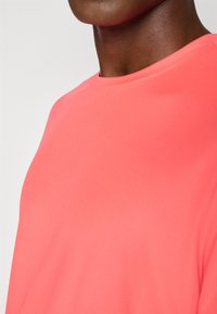 Coral performance t-shirt with a round neck, textured fabric, short sleeves, and a close fit, highlighting the smooth and breathable material.