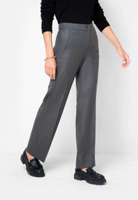Pantalon gris sur mesure à jambes droites, en tissu texturé. Il comporte une fermeture à bouton sur le devant et des poches latérales. Associé à des mocassins noirs.