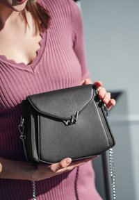 Černá kožená crossbody kabelka s klopovým zavíráním, stříbrným řetízkem a charakteristickým geometrickým logem na přední straně.