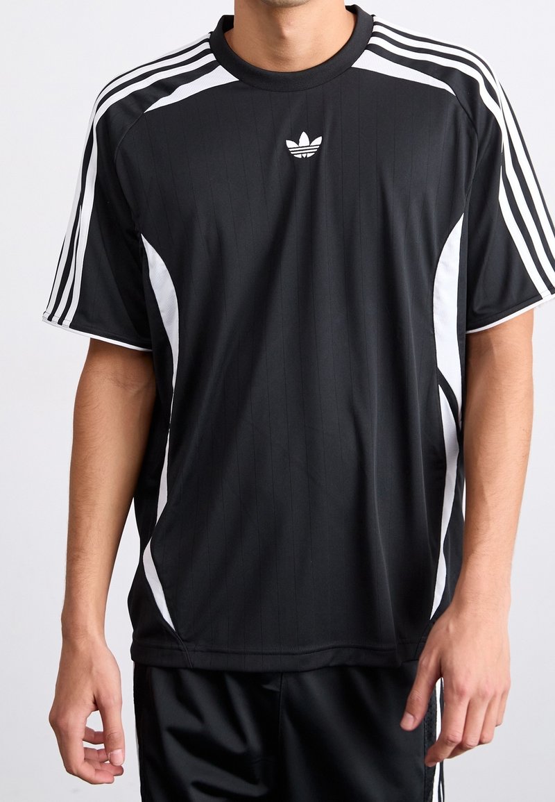 Musta urheilupaita valkoisilla yksityiskohdilla ja raidoilla. Paidassa on resorikuviointi ja pieni logo rinnassa. Lyhyet hihat, rento istuvuus.