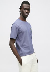 T-shirt in cotone lilla chiaro con collo rotondo e maniche corte. Presenta un piccolo logo giallo sulla tasca sul petto a sinistra.