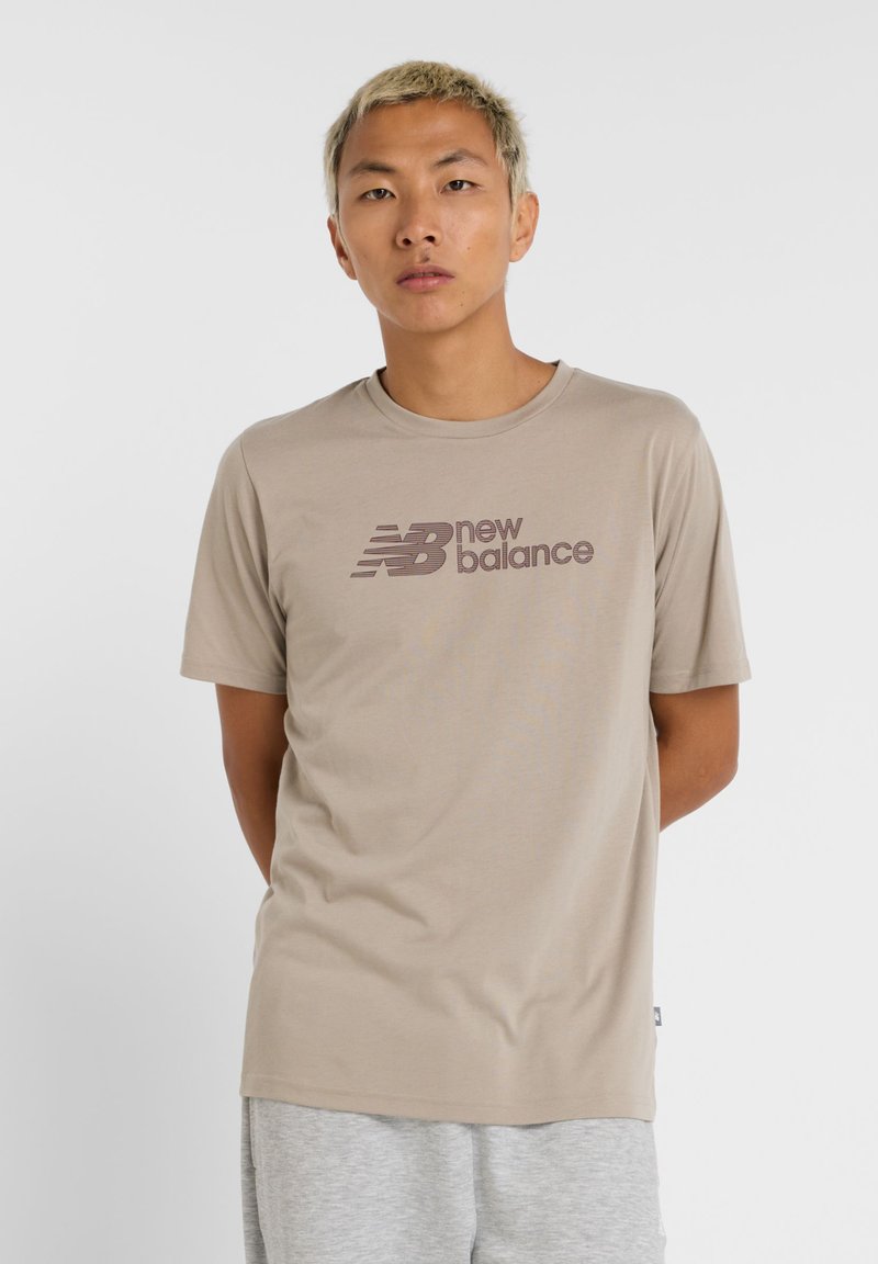 Camiseta de algodón beige con el logo de "new balance" en marrón oscuro. Manga corta, cuello redondo, textura suave, diseño minimalista.