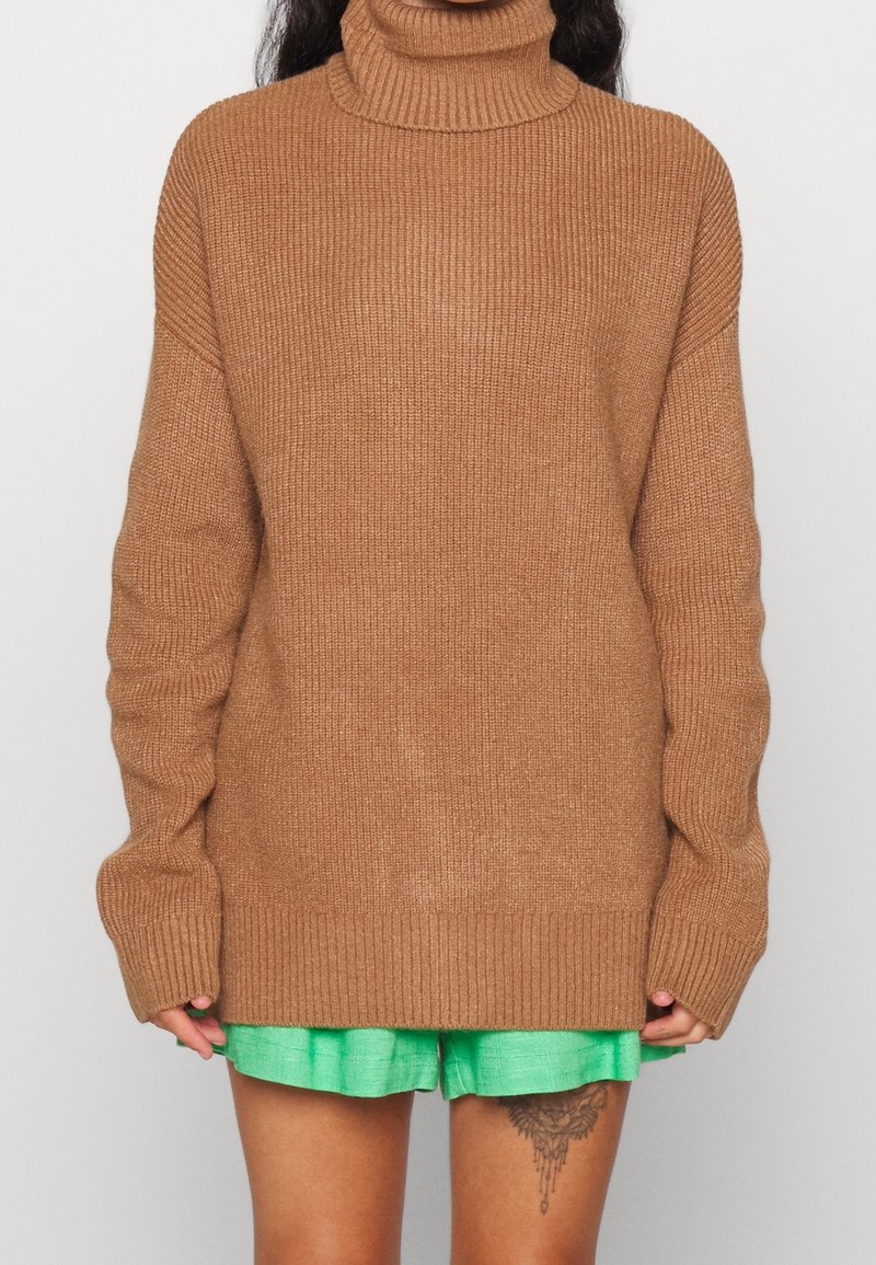 Brun ribbad polotröja med lång ärm och lös passform, i kombination med gröna shorts, som visar upp stickad textur och avslappnad design.