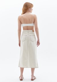Kermakosketettu denim midi-hame suoran leikkauksen kanssa, jossa on kaksi takataskua ja nahkainen etiketti vyötäröllä. Minimalistinen muotoilu ilman koristeita.