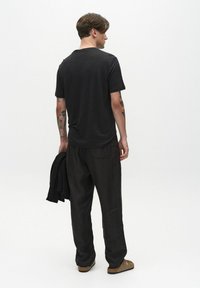 Fekete, crew neck női póló, laza szabással, melyet laza, sötét nadrággal párosítanak. A modell egy összehajtott ruhadarabot tart, kiemelve a finom varrási részleteket.