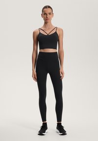 Crni atletski crop top s ukriženim trakama uparen s crnim hlačama visokog struka. Obje stavke sadrže glatku, rastezljivu tkaninu.