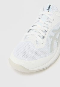 Gros plan sur une chaussure de course Asics blanche avec une mesh respirante, des lacets blancs et un logo de la marque argenté sur le côté.