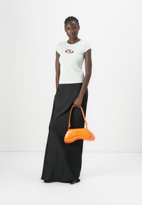Tricou ajustat de culoare albastru deschis cu un logo mic decupat, asociat cu o fustă maxi neagră și o geantă lucioasă portocalie cu design curbat.