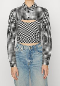 Černobílá kostkovaná zkrácená košile s dlouhými rukávy, límečkem a předním výřezem, spárovaná s vysoce pasovými světle modrými džíny.