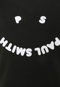 Černé tričko s krátkými rukávy a velkým hravým bílým textem, který vytváří nápis "PAUL SMITH" v zakřiveném, rozmarném písmu.