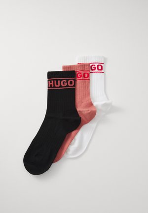 Three pairs of ribbed socks in black, pink, and white, each featuring a red "HUGO" logo on the cuff. Soft fabric with a snug fit.