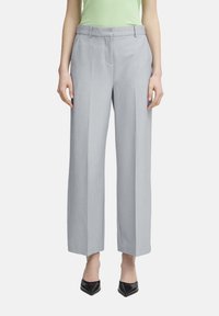 Pantalons larges gris clair en tissu lisse, avec une taille plate, des passants de ceinture et des plis marqués, associés à des talons noirs.