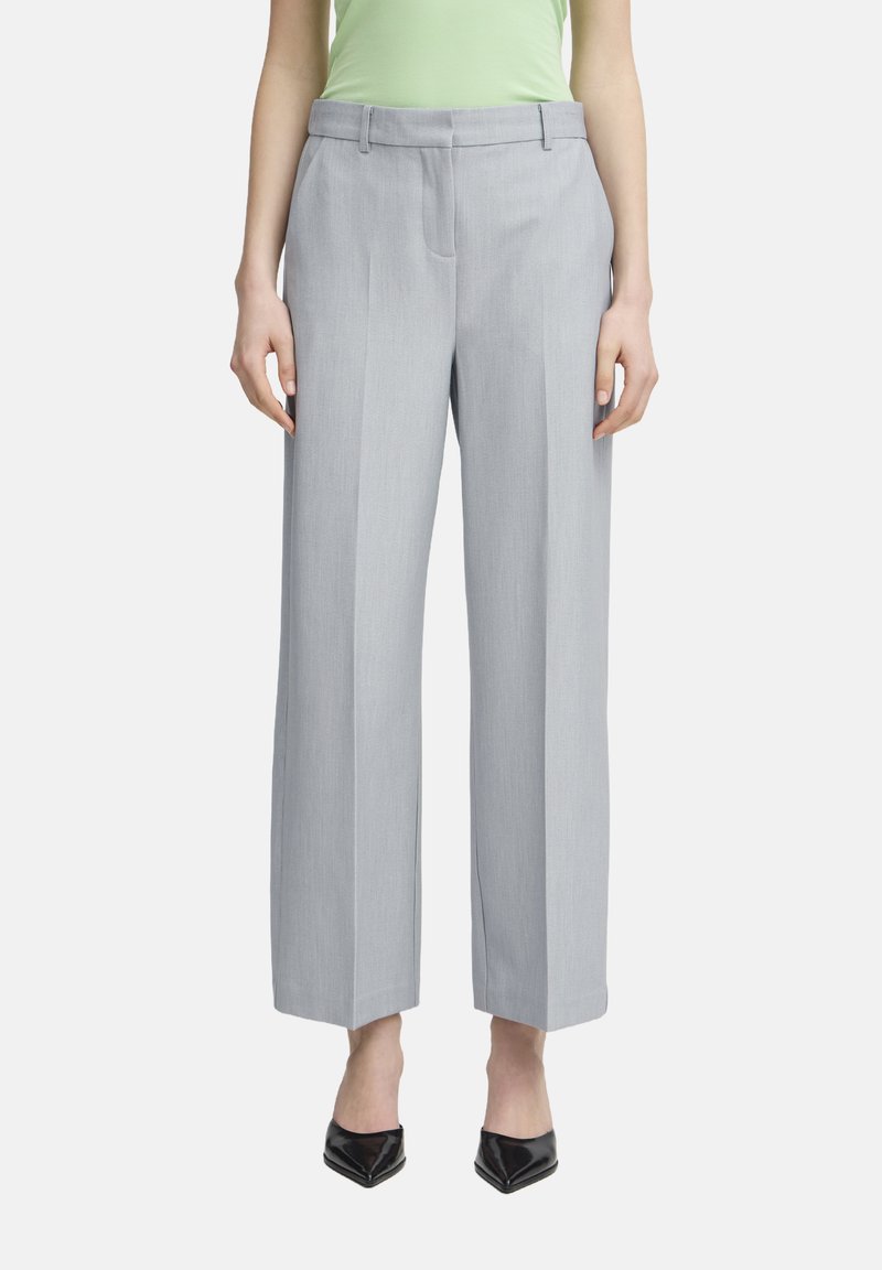 Pantalons larges gris clair en tissu lisse, avec une taille plate, des passants de ceinture et des plis marqués, associés à des talons noirs.