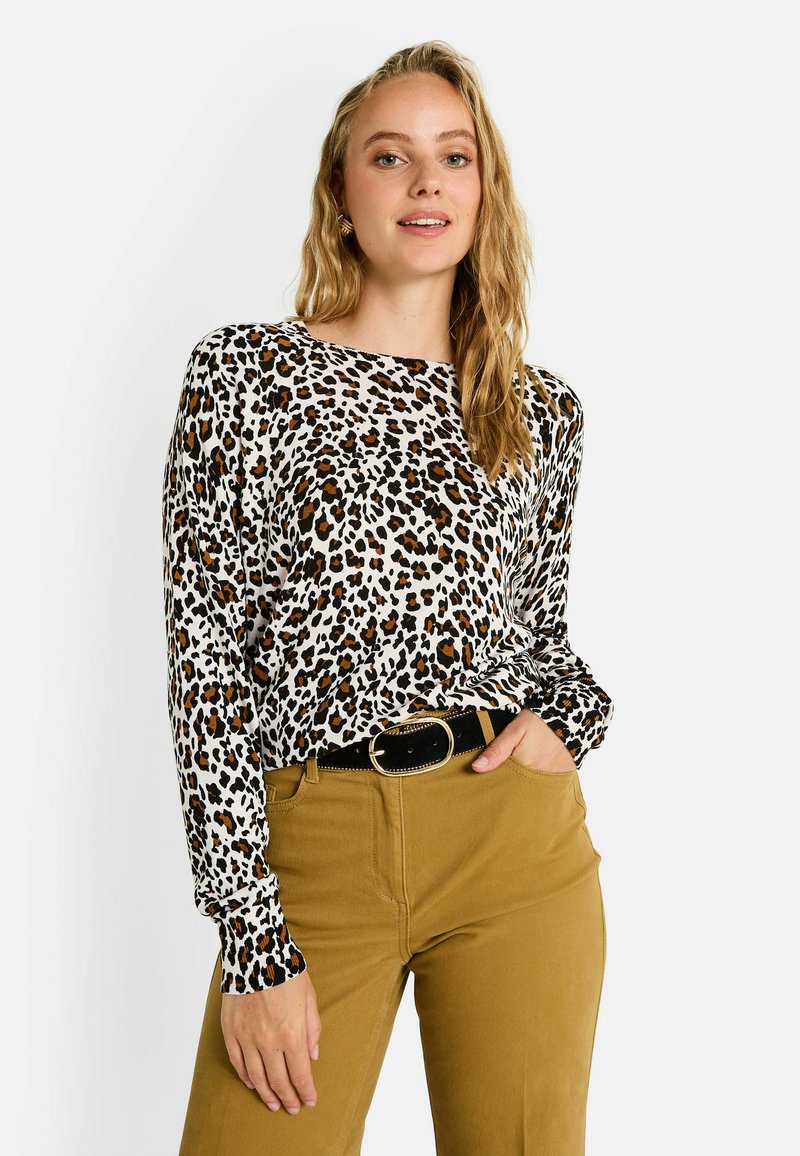 Top de manga larga en blanco con estampado de leopardo negro y naranja, combinado con pantalones en color mostaza y un cinturón negro con una hebilla redonda.