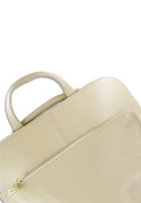 Sac à main en cuir beige avec une finition texturée, un haut arrondi et une poche zippée. Dispose d'une poignée courte pour un transport facile.