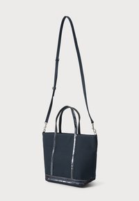Bolso de lona navy con dos asas cortas y una correa de hombro ajustable. Presenta detalles metálicos a lo largo de los bordes.