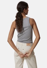 Camiseta sin mangas de algodón gris con un escote redondo, diseño ajustado y un acabado texturizado, combinada con pantalones de color crema que presentan una etiqueta de cuero.