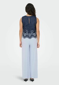 Top senza maniche color navy con orlo in pizzo floreale ricamato, abbinato a pantaloni a gamba larga azzurri. Dettaglio sulla schiena a forma di chiave e texture morbida.