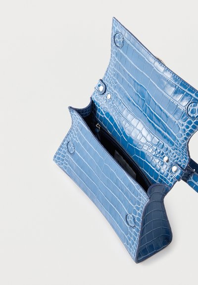 Sac à main bleu clair avec motif crocodile, rabat ouvert et poche intérieure zippée visible sur fond blanc uni.