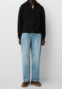 Svart stickad tröja med dragkedja i kragen, kombinerad med ljusblå jeans med raka ben och bruna platåskor med texturerad sula.