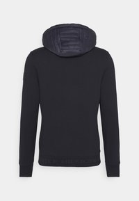 Svart sweatshirt med en kviltad marinblå huva, ribbade ärmslut och nederkant. Har en tonad logotyp längs den undre kanten. Slät textur.